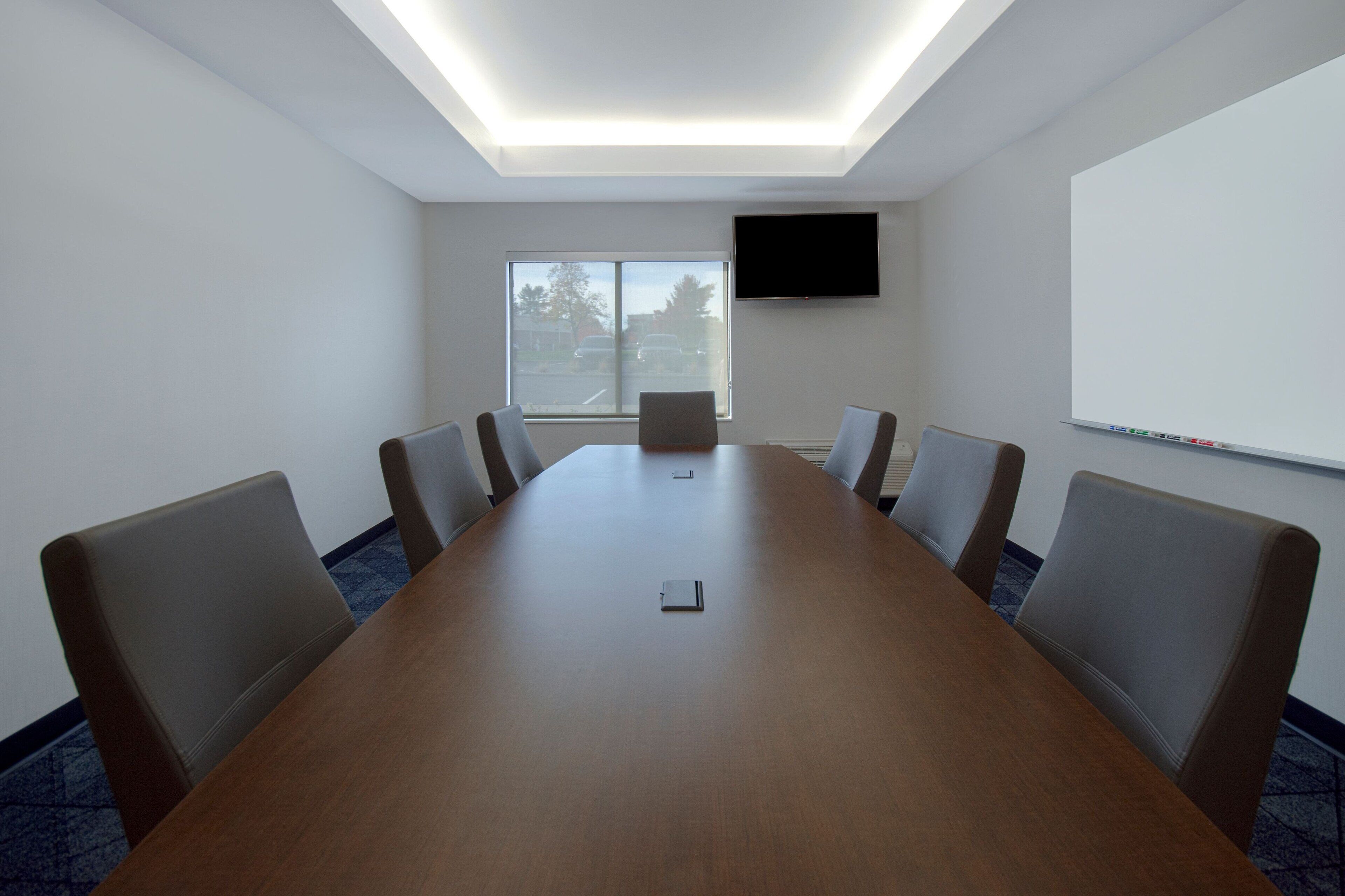 Uma sala de conferências com uma mesa comprida, seis cadeiras, uma TV de tela plana e um quadro branco.