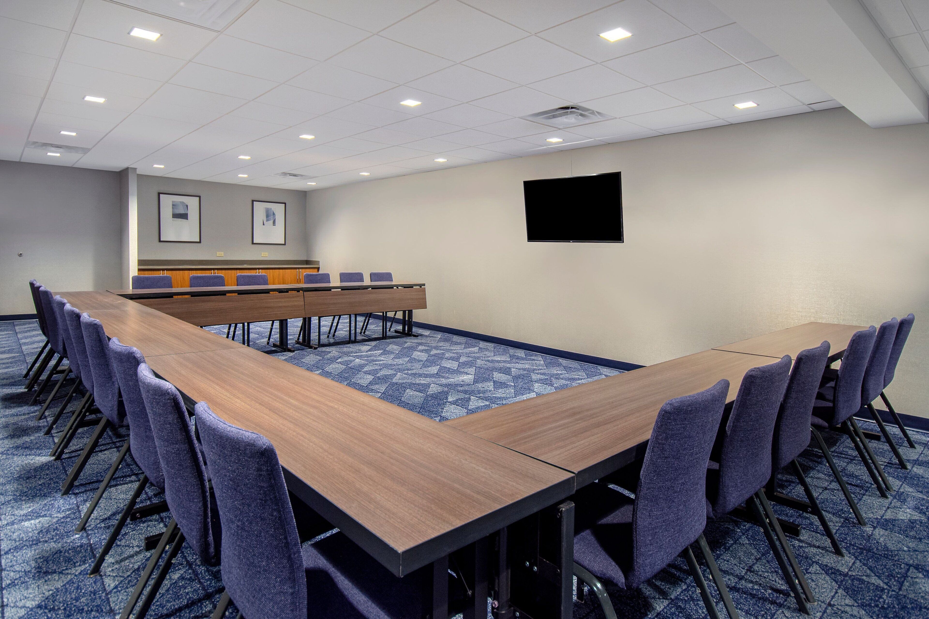 Une salle de conférence avec une longue table, des chaises, un téléviseur à écran plat et des tableaux accrochés au mur.