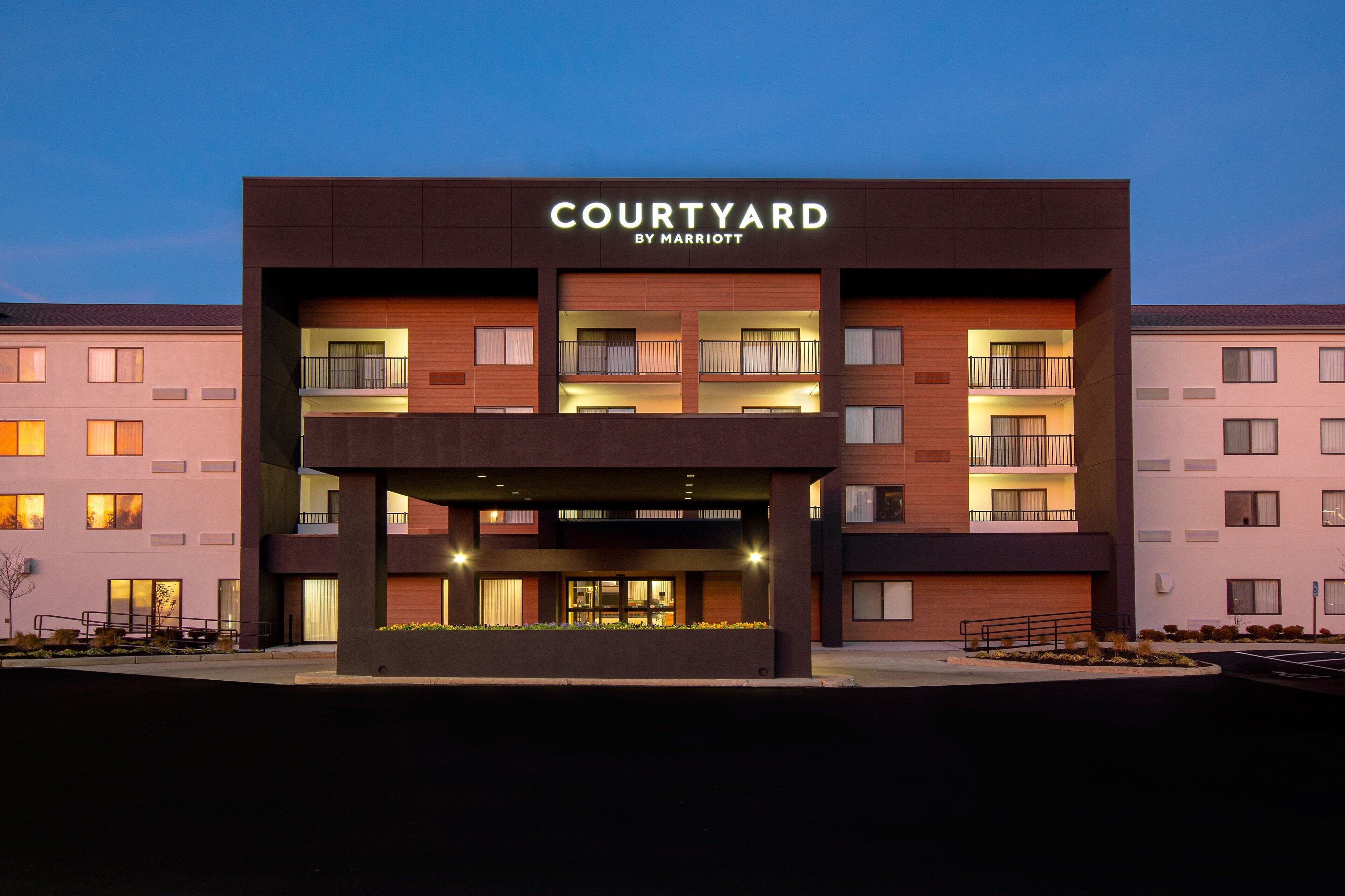 Un hotel Courtyard by Marriott con diseño moderno, varios balcones y una zona de entrada cubierta.