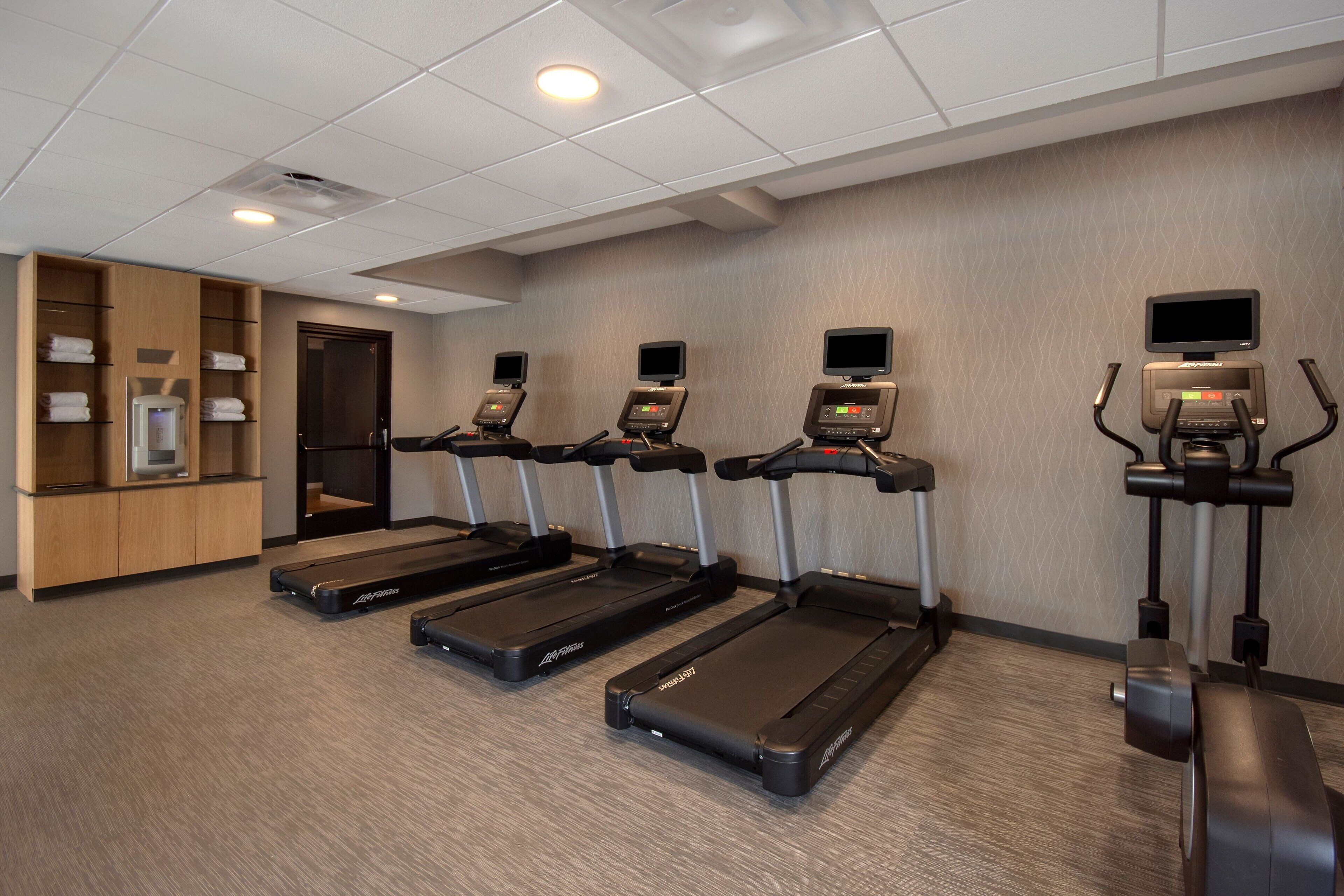Un gimnasio con cuatro cintas de correr, un televisor montado en la pared y un dispensador de agua.