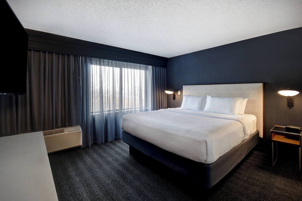 A hotel room with a large bed, a flat-screen TV, a desk, and a window with curtains.