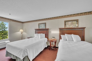 A hotel room with two beds, a bedside table with a lamp, a small round table with a phone, and a window with a view of trees. - Gray Inn and Suites (Gray)