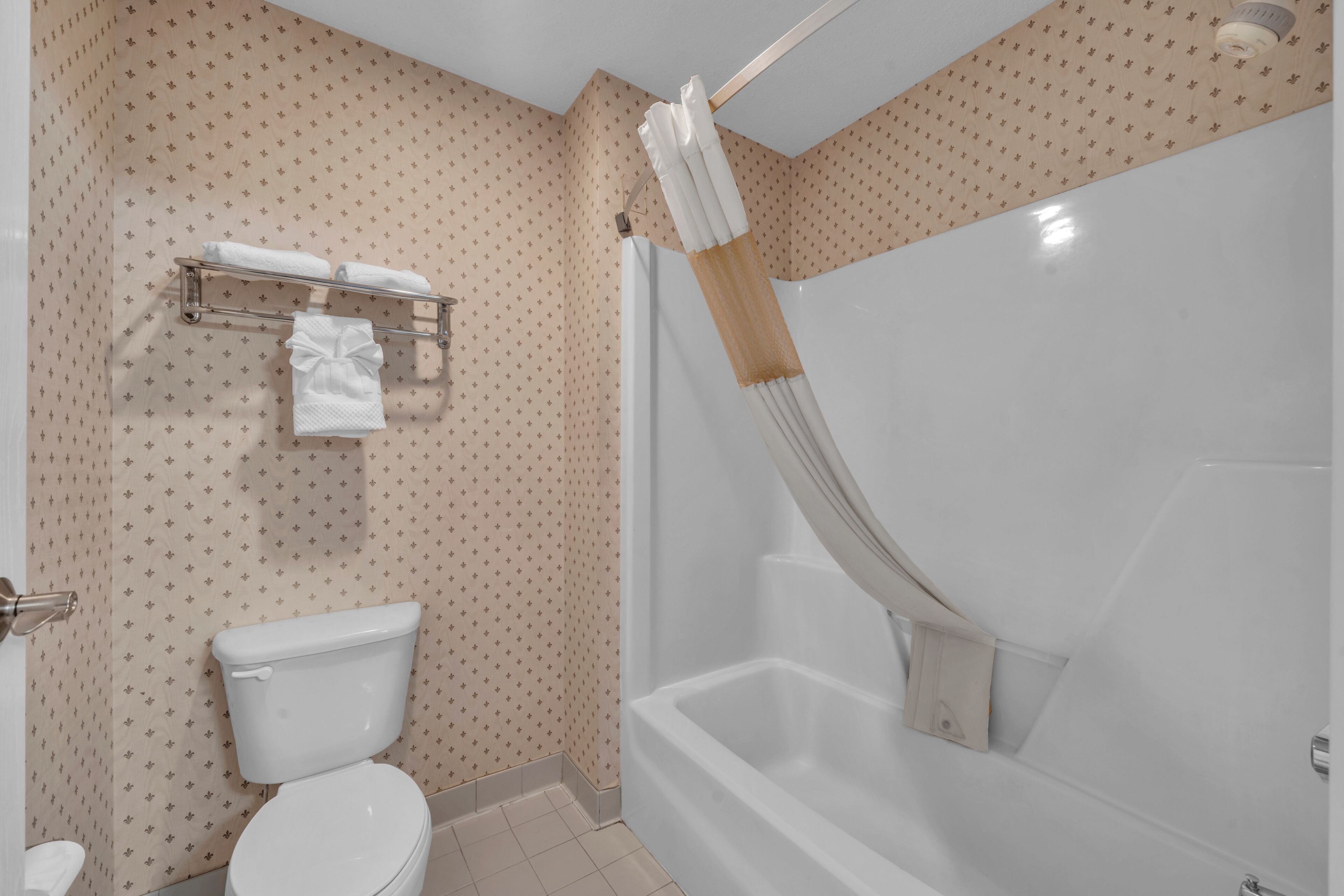 A bathroom with a toilet, a shower with a curtain, and a towel rack with towels.