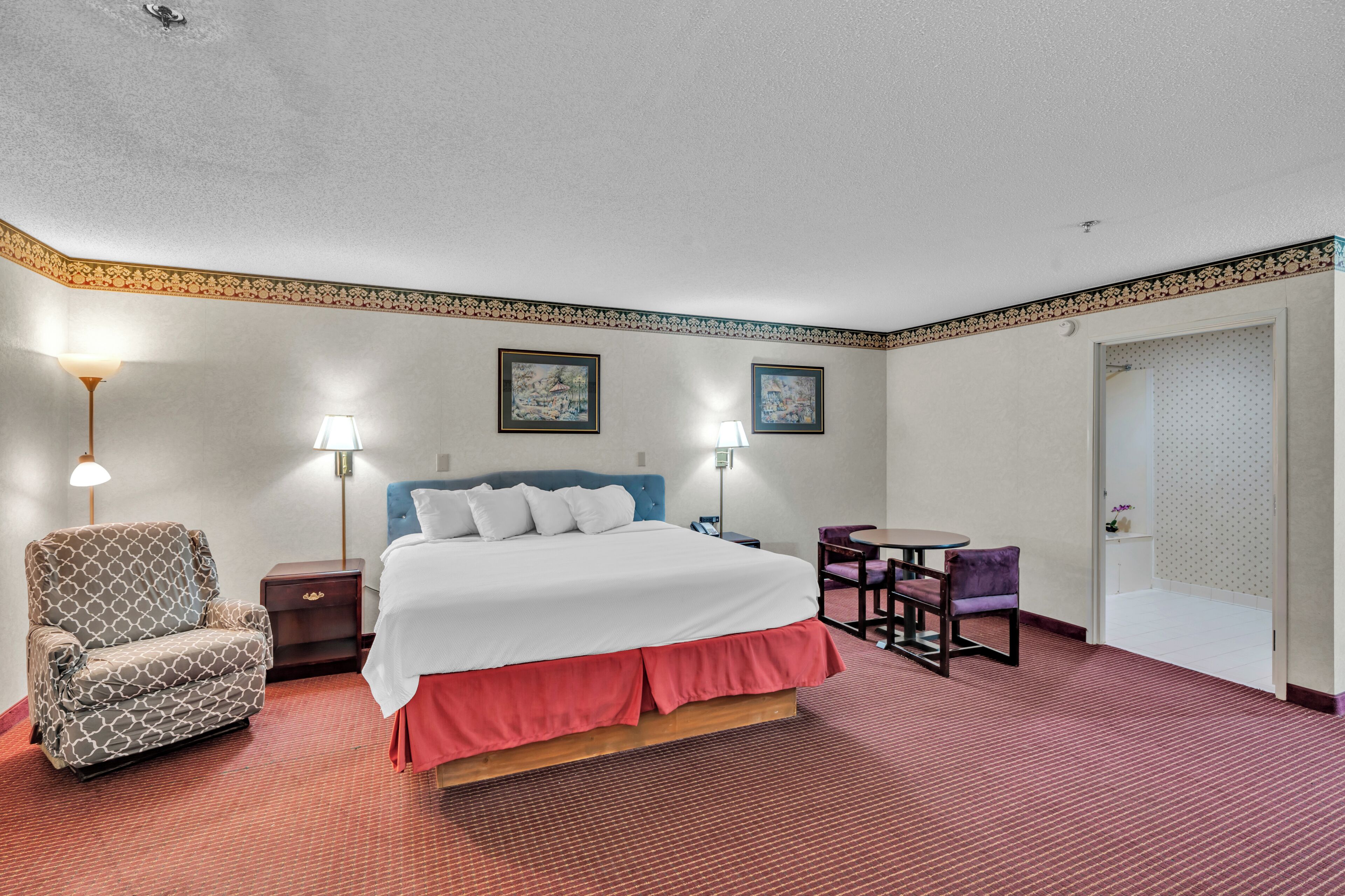 A hotel room with a bed, a chair, a desk, and two lamps.