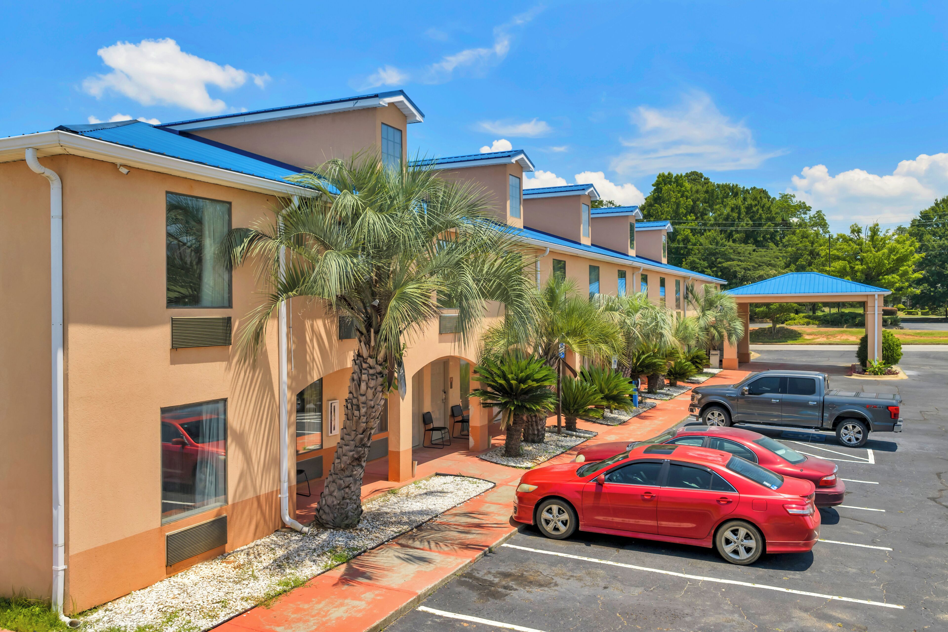 A hotel with a row of rooms, a parking lot, and a covered area.