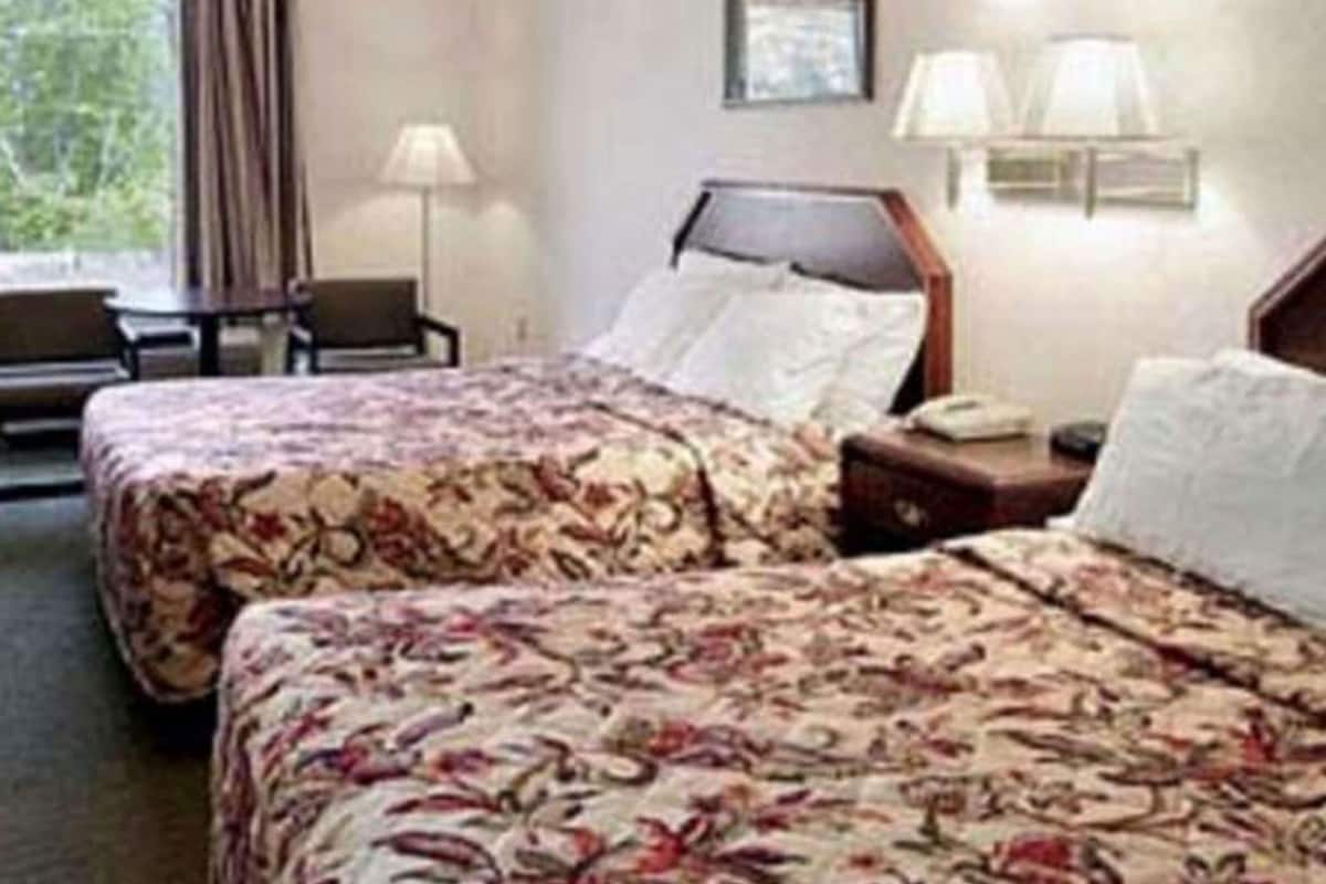 Quarto de hotel com duas camas, uma mesa, uma cadeira e uma janela com cortinas.