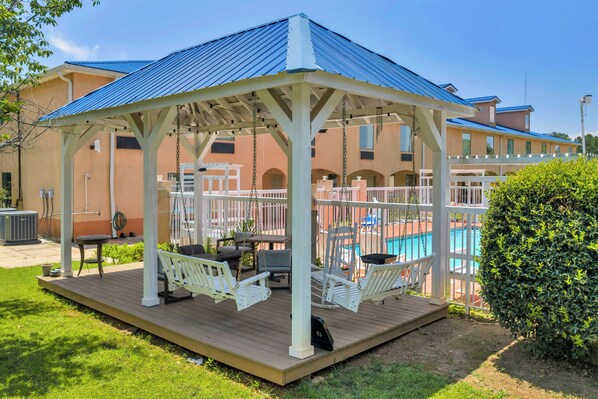 A covered outdoor area with a pool, seating, and a pergola structure. - Gray Inn and Suites (Gray)