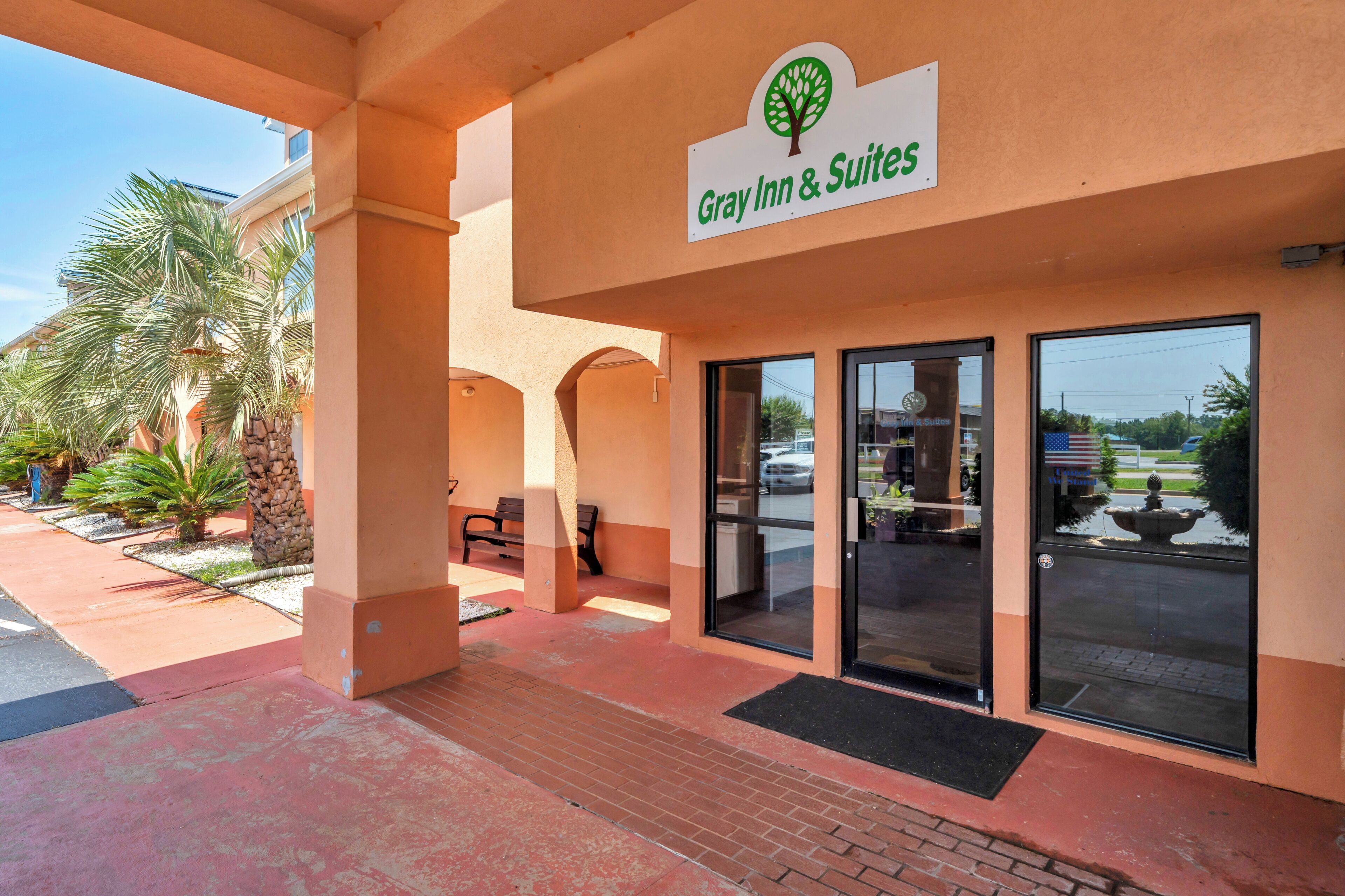 A hotel entrance with a sign reading 'Gray Inn & Suites,' palm trees, and a clear sky.