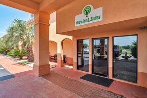 Entrada de un hotel con un letrero que dice 'Gray Inn & Suites', palmeras y un cielo despejado.