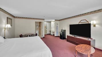 A hotel room with a large bed, a TV, a small table, a desk, and a bathroom visible through an open door.