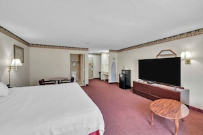 Habitación de hotel con una cama grande, televisor, una mesita, escritorio y baño visible a través de una puerta abierta.