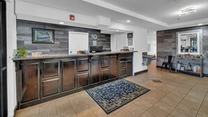 A modern kitchen with dark wood cabinets, a granite countertop, and a blue patterned rug. - Gray Inn and Suites (Gray)