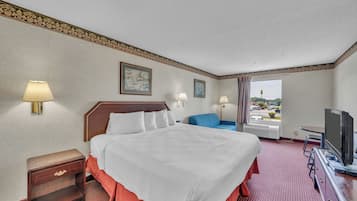A hotel room with a bed, a desk with a television, a chair, a nightstand, and a window with a view.