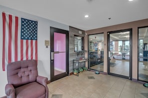 A hotel lobby with an American flag, a pink door, a glass door leading to a dining area, and a chair. - Gray Inn and Suites (Gray)