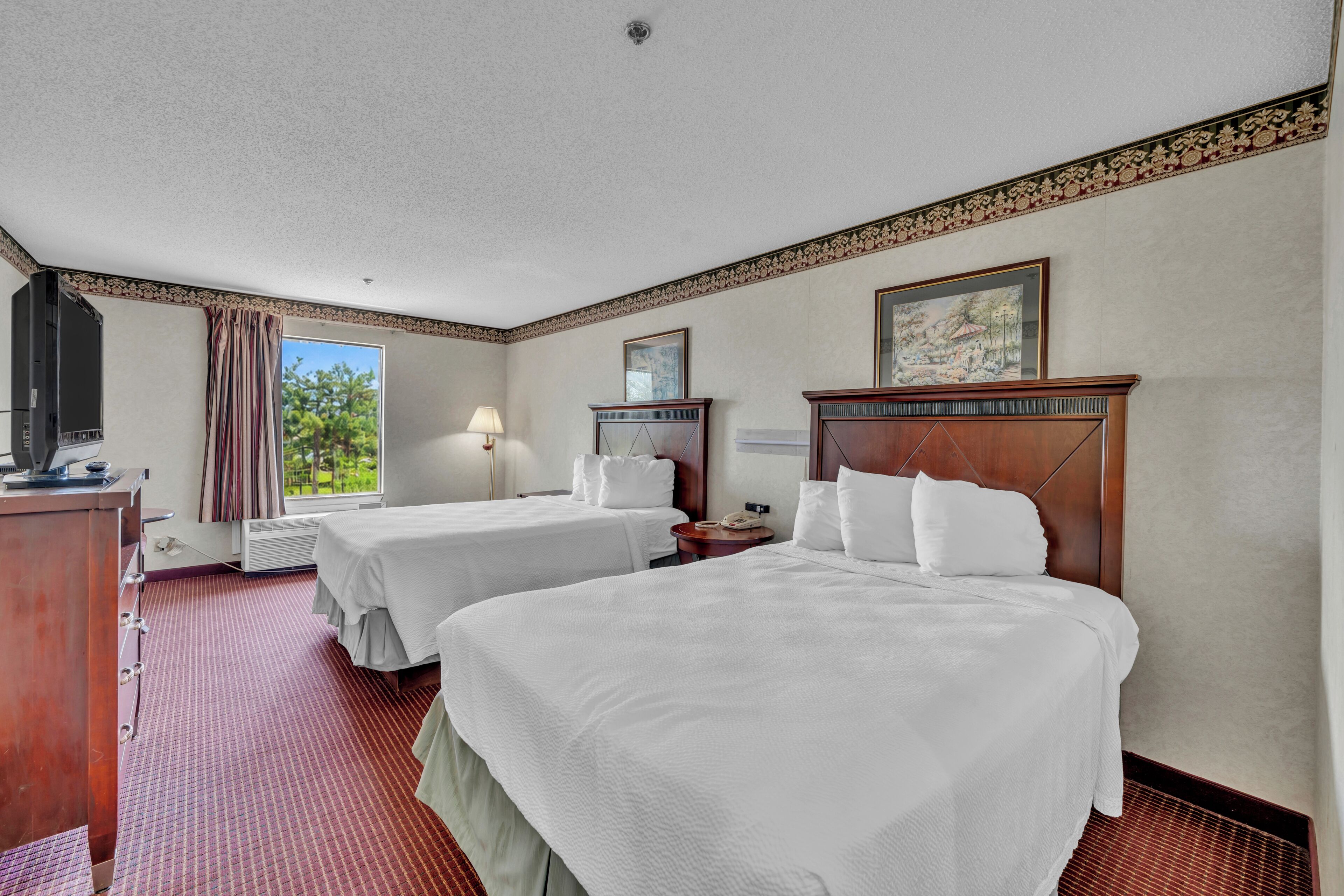 A hotel room with two beds, a desk, a lamp, a TV, and a window with curtains.