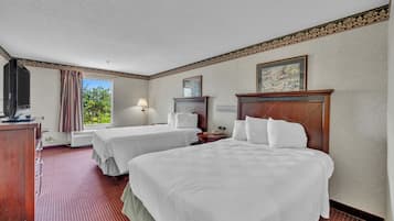 A hotel room with two beds, a desk, a lamp, a TV, and a window with curtains.