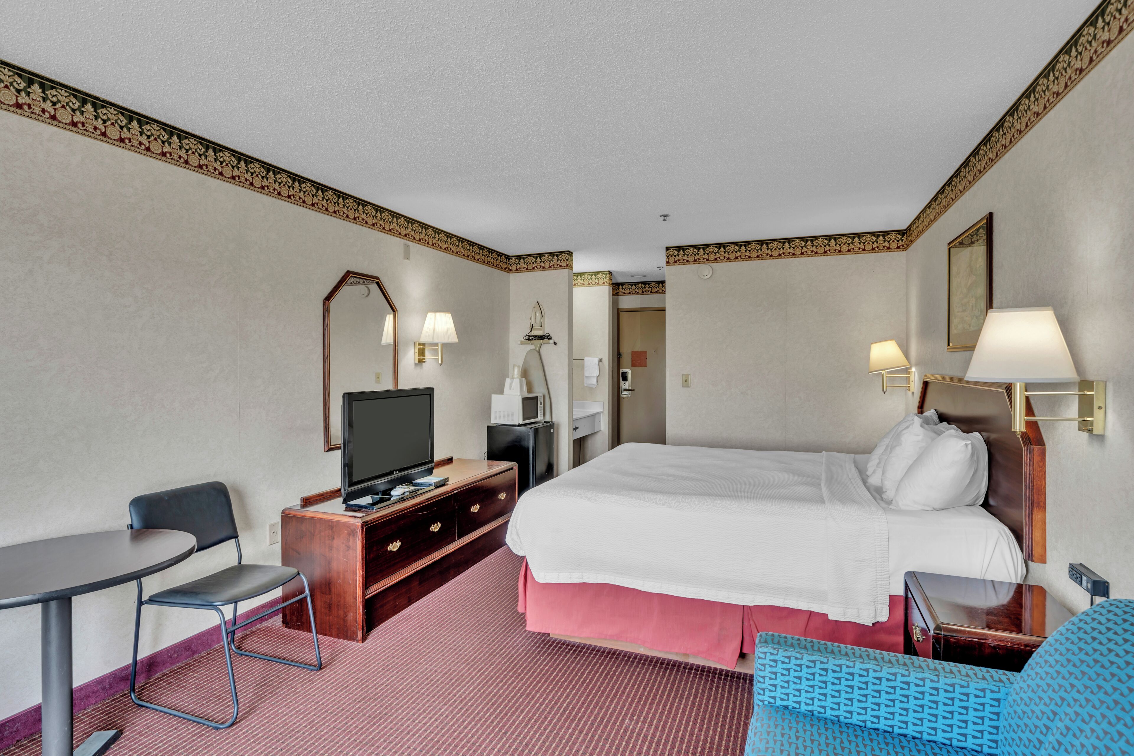 A hotel room with a bed, a desk, a chair, a television, and a mirror.