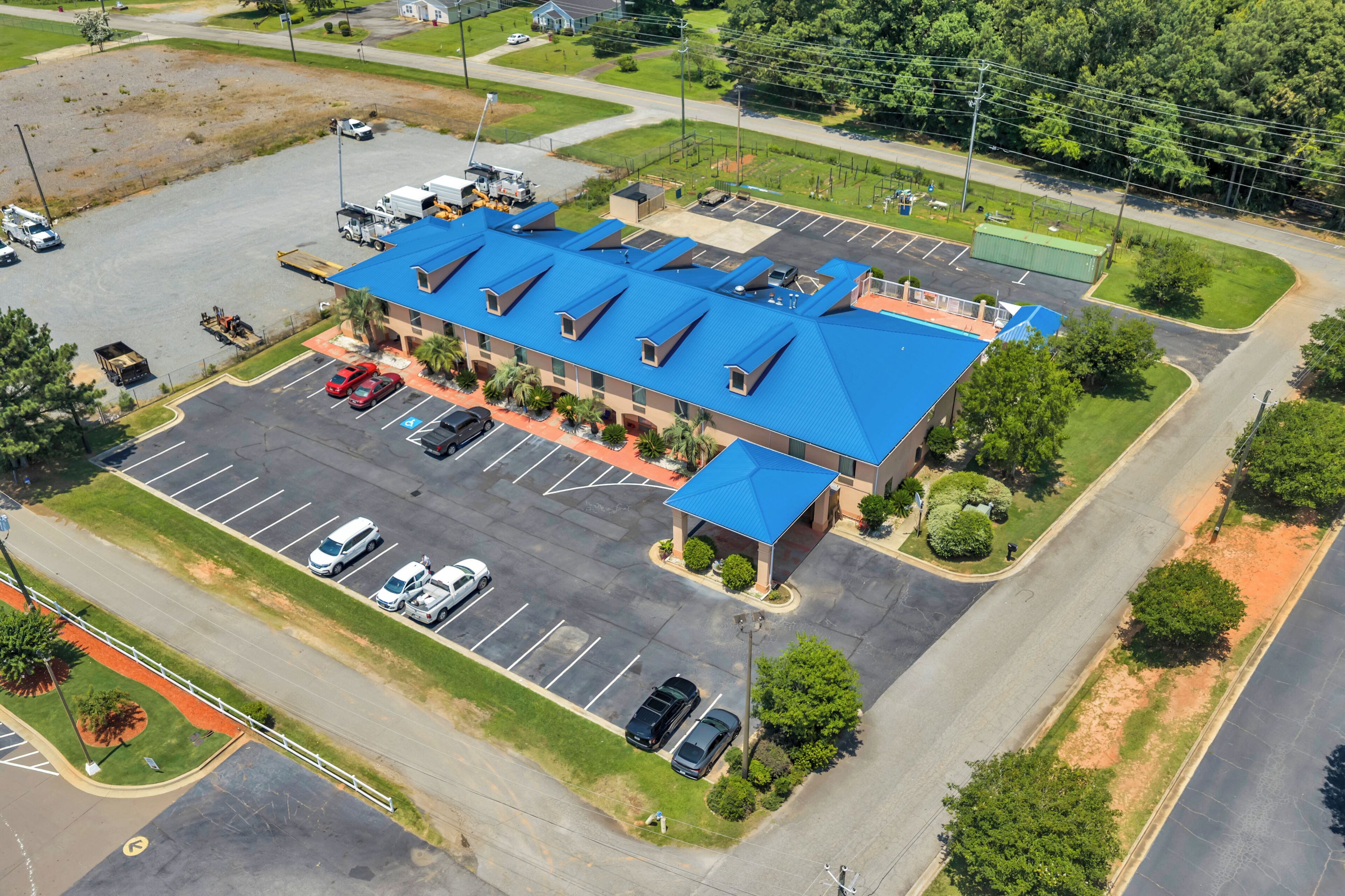 An aerial view of a hotel with a blue roof, a parking lot, and surrounding greenery.