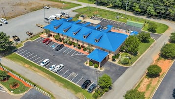 An aerial view of a hotel with a blue roof, a parking lot, and surrounding greenery.