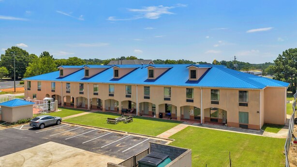 A multi-story hotel with a blue roof, a parking lot, and a grassy area. - Gray Inn and Suites (Gray)