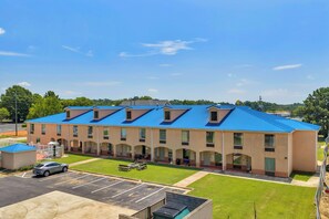 A multi-story hotel with a blue roof, a parking lot, and a grassy area. - Gray Inn and Suites (Gray)