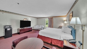A hotel room with a bed, a desk with a telephone, a television, a sofa, and a small refrigerator. - Gray Inn and Suites (Gray)