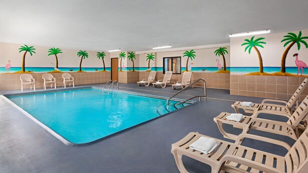 An indoor swimming pool with lounge chairs and palm tree murals on the walls. - Days Inn by Wyndham Kansas City International Airport (Kansas City)
