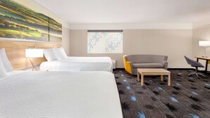 A hotel room with two beds, a gray armchair, a small table, and a window with a view of a landscape. - Days Inn by Wyndham Kansas City International Airport (Kansas City)