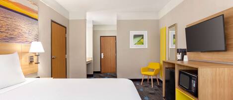 Habitación de hotel con cama, escritorio, televisor de pantalla plana, microondas, silla y puerta que da a otra habitación.