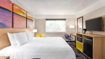 A hotel room with a large bed, a desk with a chair, a television, and artwork on the wall.