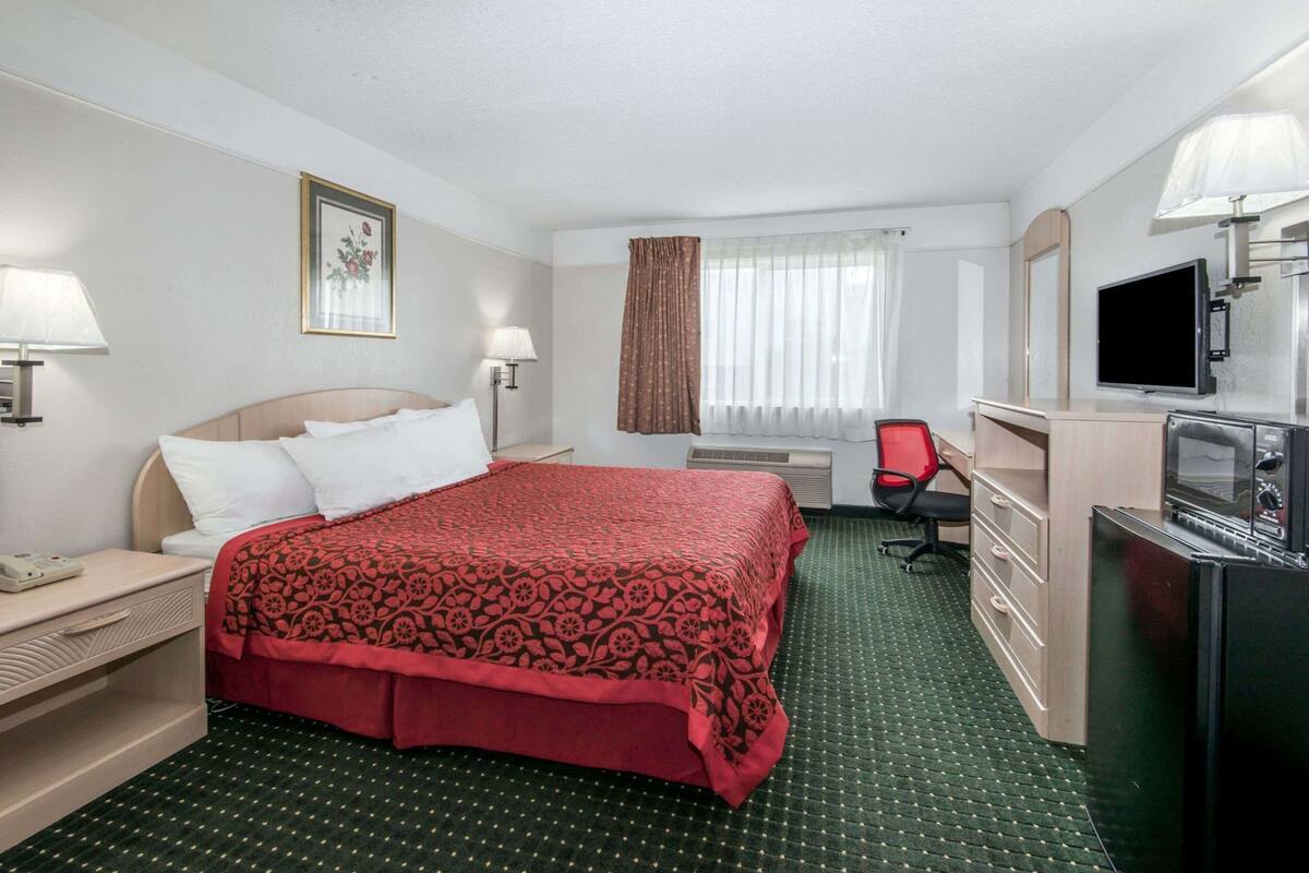 Ein Hotelzimmer mit Bett, Schreibtisch mit Telefon, Stuhl, Fernseher und Minibar.