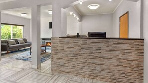 A modern reception area with a stone-textured counter, a sofa, and a fireplace. - Days Inn by Wyndham Kansas City International Airport (Kansas City)