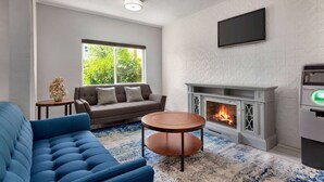 A modern living room with a fireplace, a sofa, a blue armchair, and a round coffee table. - Days Inn by Wyndham Kansas City International Airport (Kansas City)