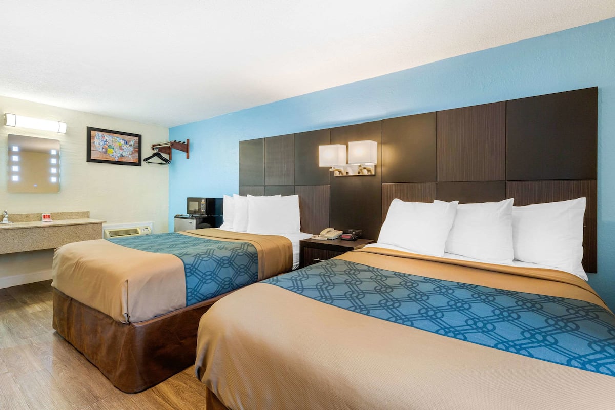 A hotel room with two beds, a bathroom, and a small desk with a telephone.