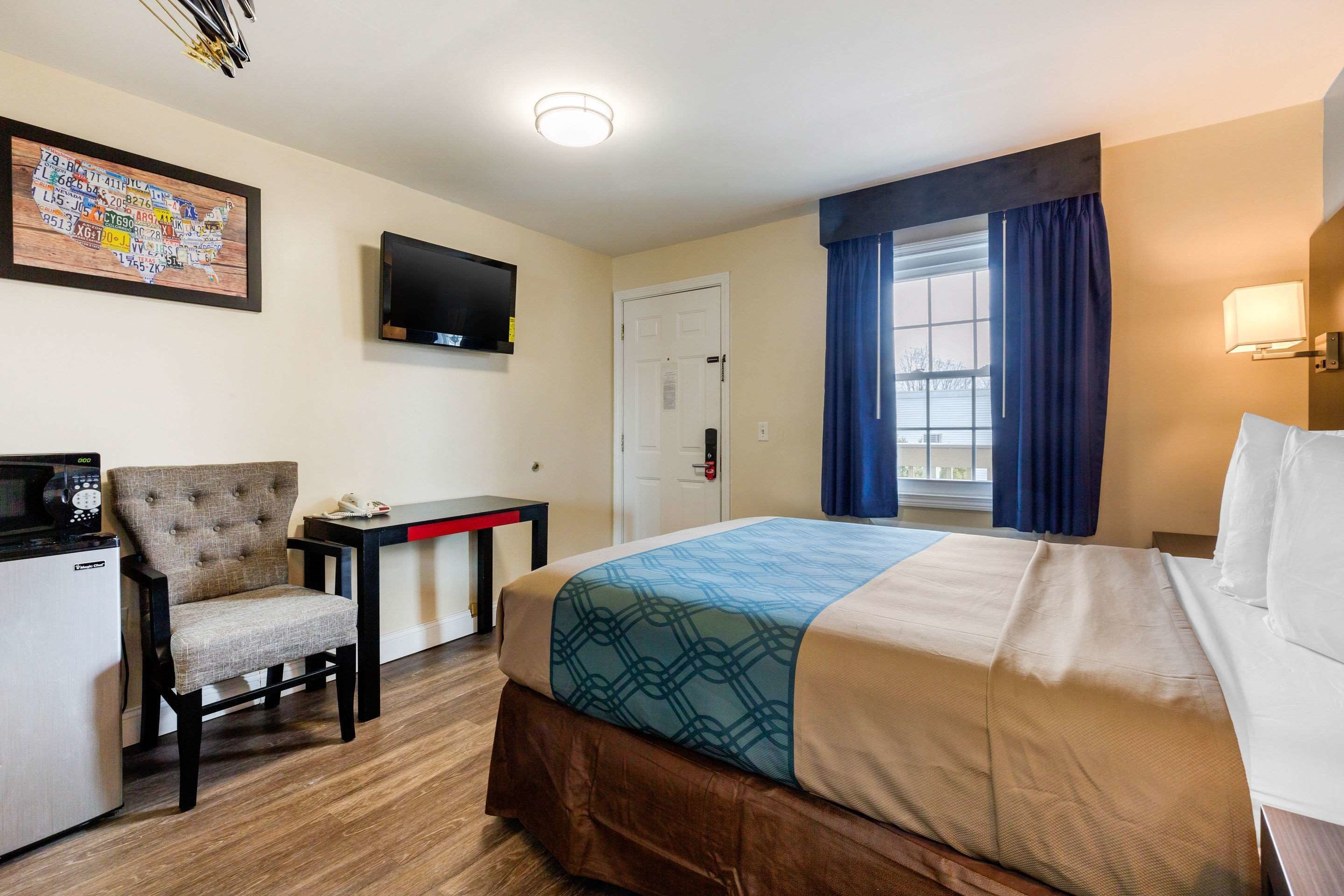 A hotel room with a bed, a desk, a chair, a television, and a map on the wall.