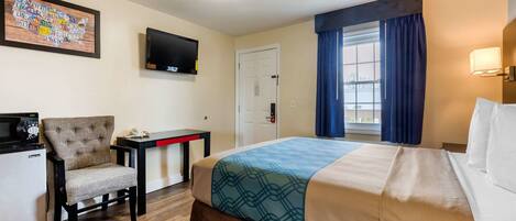 A hotel room with a bed, a desk, a chair, a television, and a map on the wall.