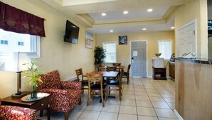 A dining area with a table and chairs, a sofa, a TV mounted on the wall, and a plant on a table. - Econo Lodge West Yarmouth on Cape Cod (West Yarmouth)