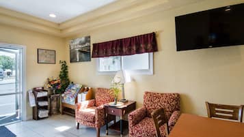 A hotel room with a dining area, a TV mounted on the wall, and a window with a view of the outside.