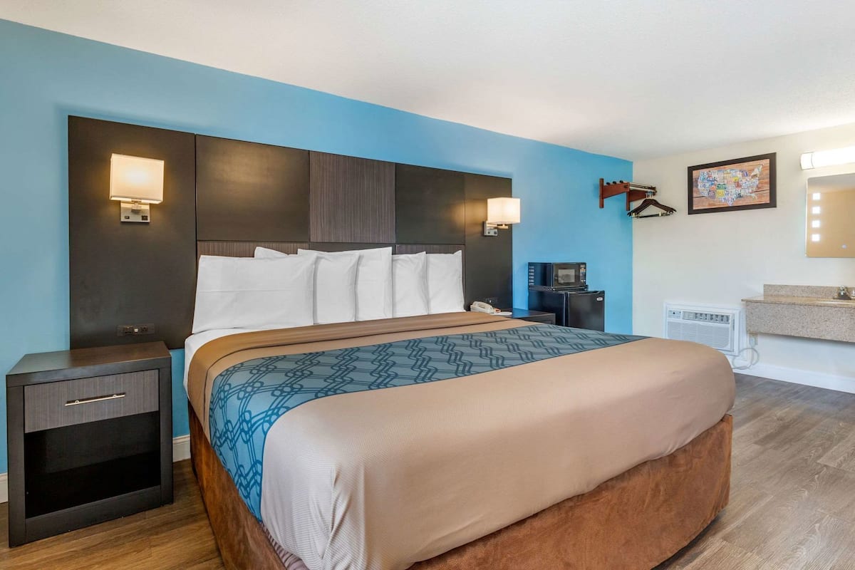 A hotel room with a large bed, bedside tables, a desk, a microwave, and a small refrigerator.