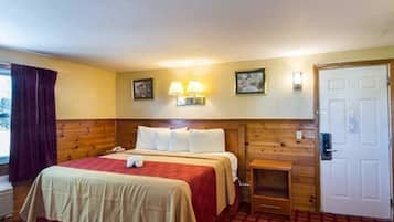 Hotelkamer met een houten hoofdeinde, een bed met een rood en beige dekbedovertrek, twee wandlampen, een klein houten nachtkastje en een deur met een handgreep.