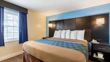 Ein Hotelzimmer mit einem großen Bett, einem Nachttisch, einer Lampe und einem Fenster mit Vorhängen.