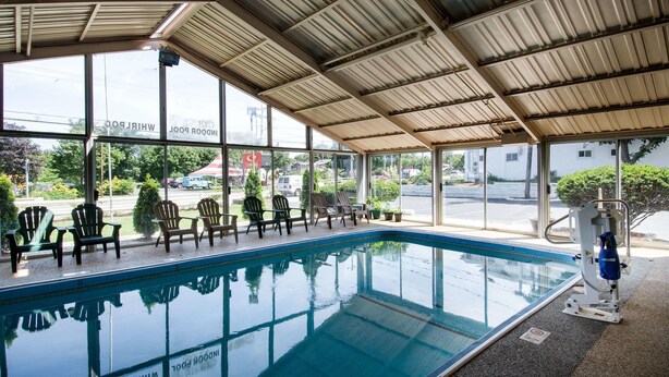 An indoor swimming pool with clear glass walls, a metal roof, and several Adirondack chairs around the pool. - Econo Lodge West Yarmouth on Cape Cod (West Yarmouth)