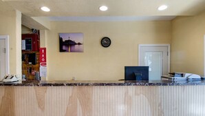 A reception area with a wooden reception desk, a clock, a framed picture, and a door. - Econo Lodge West Yarmouth on Cape Cod (West Yarmouth)