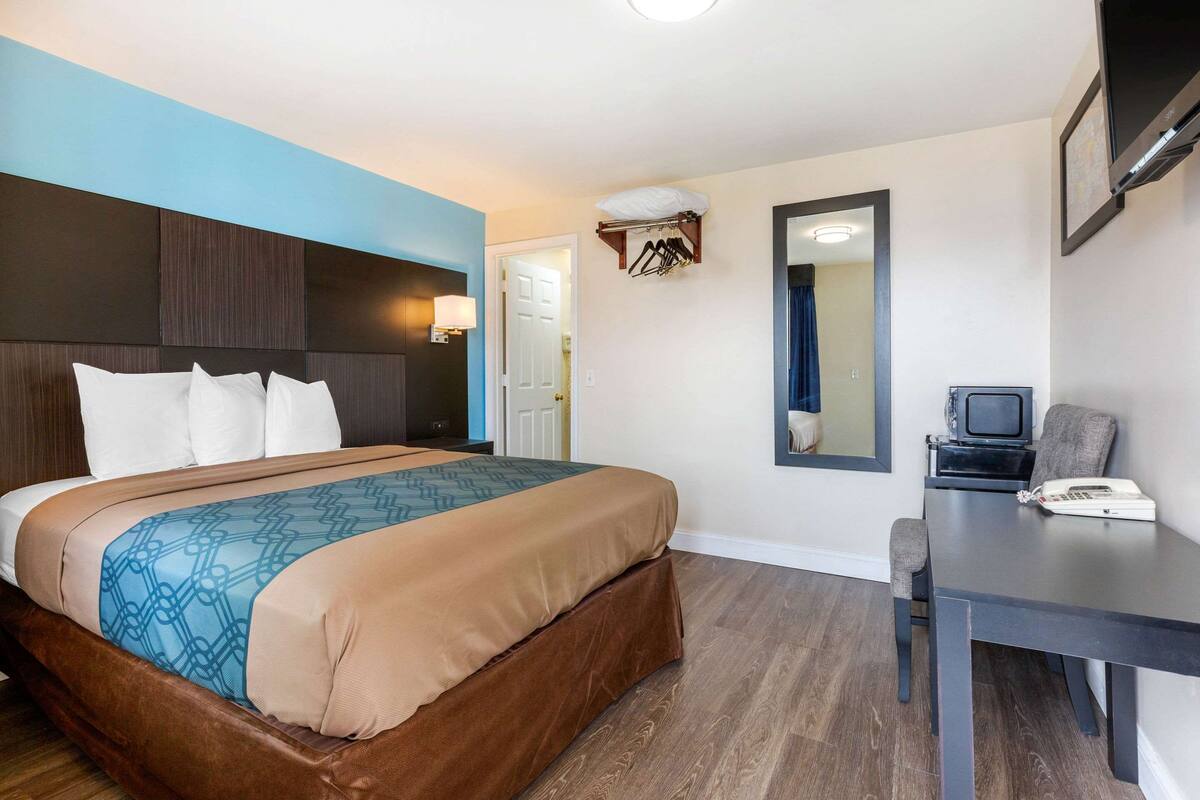 A hotel room with a bed, a desk, a television, and a mirror.