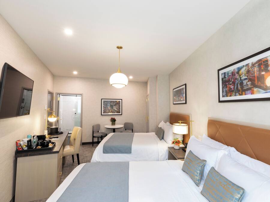 Une chambre d’hôtel avec deux lits, un bureau, une chaise, une petite table et un téléviseur.