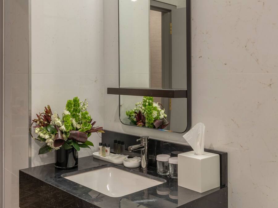 A modern bathroom with a black marble sink, a large mirror, and a vase of flowers.