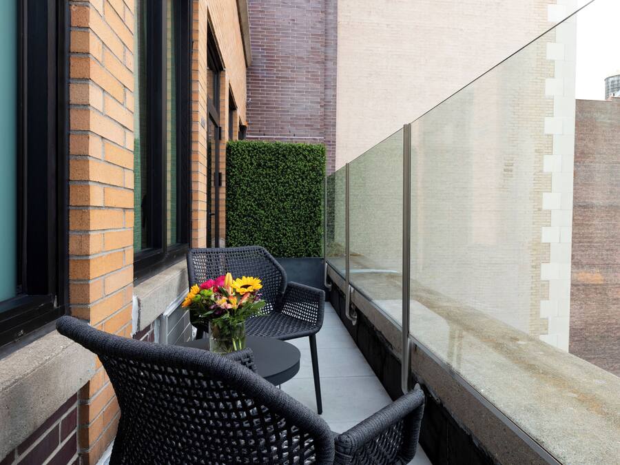 A balcony with two wicker chairs, a small round table, and a vase with flowers.