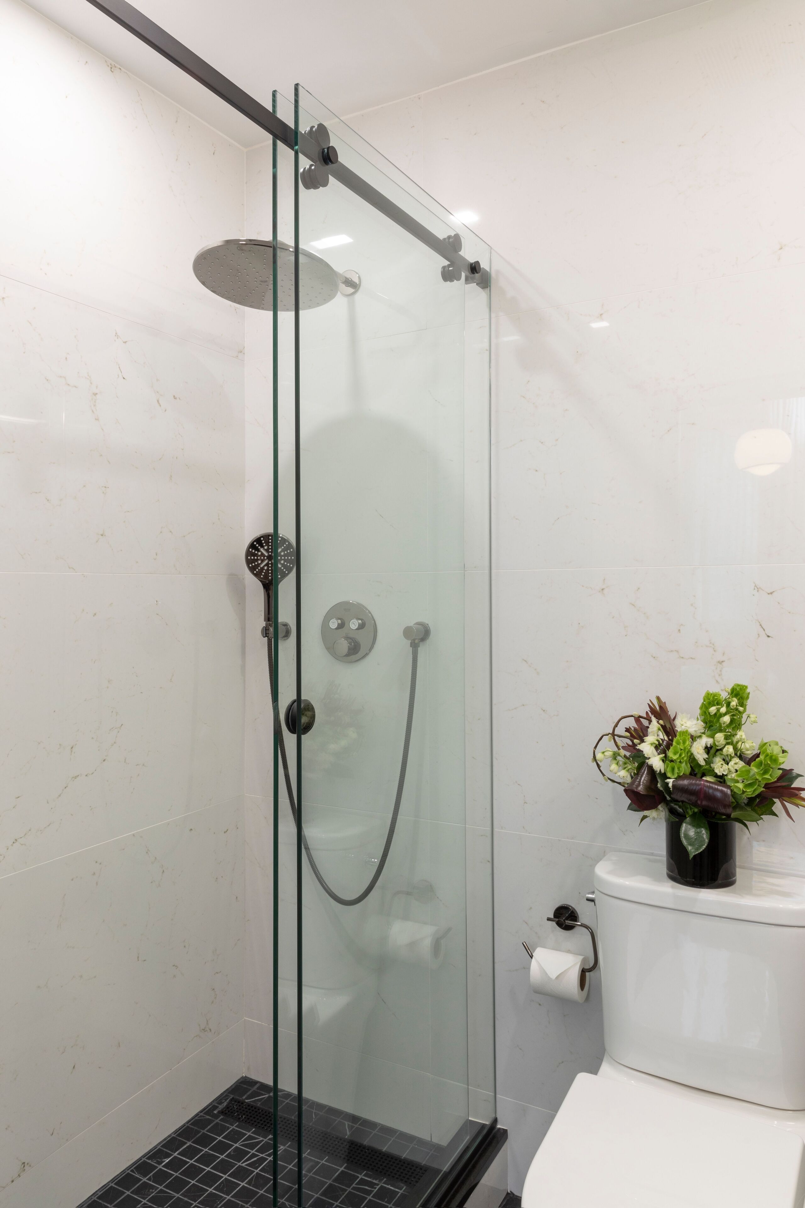 A glass-enclosed shower with a handheld showerhead and a wall-mounted faucet.
