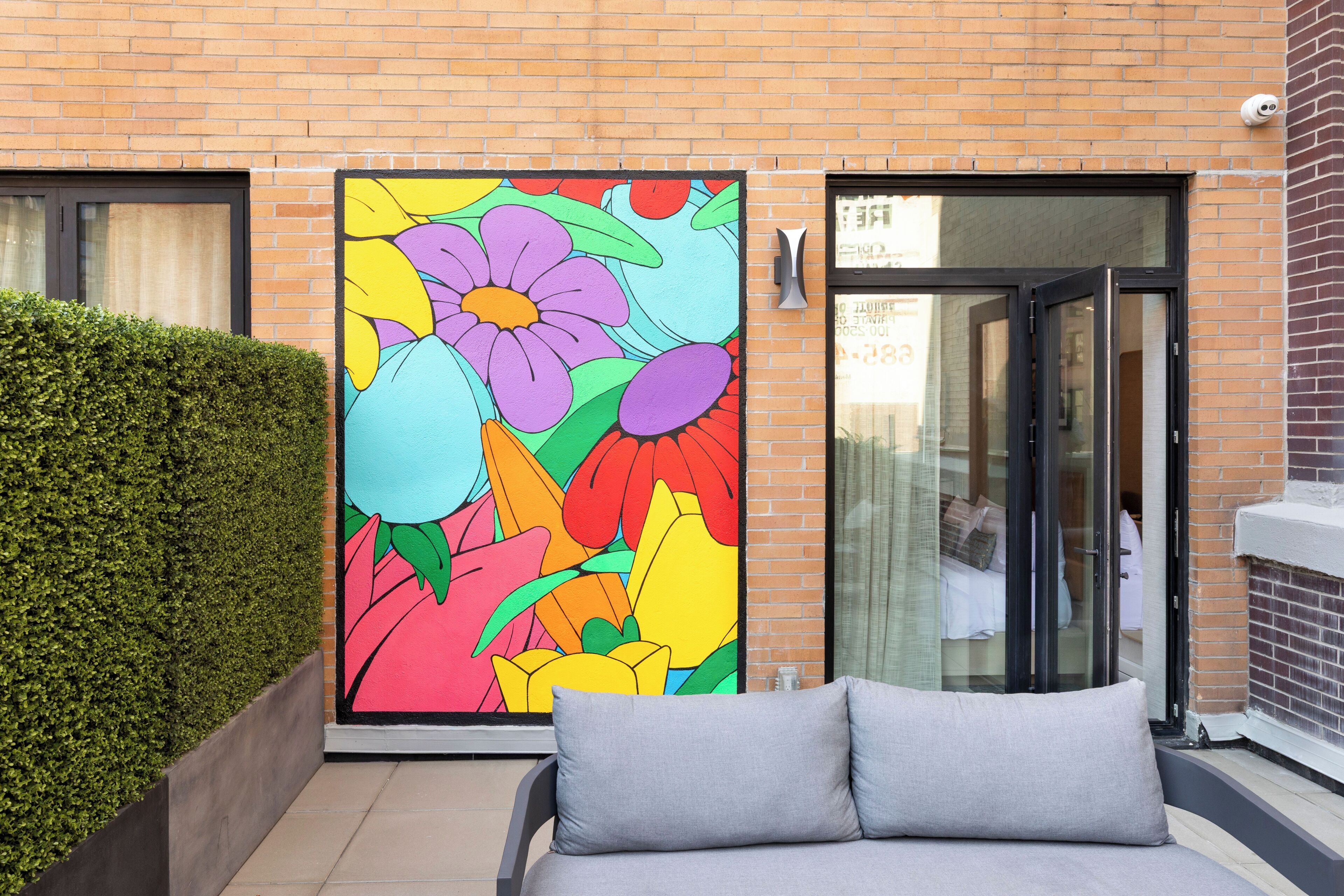 Un edificio moderno con un mural de flores coloridas, una entrada de puerta de cristal y un sofá gris en primer plano.