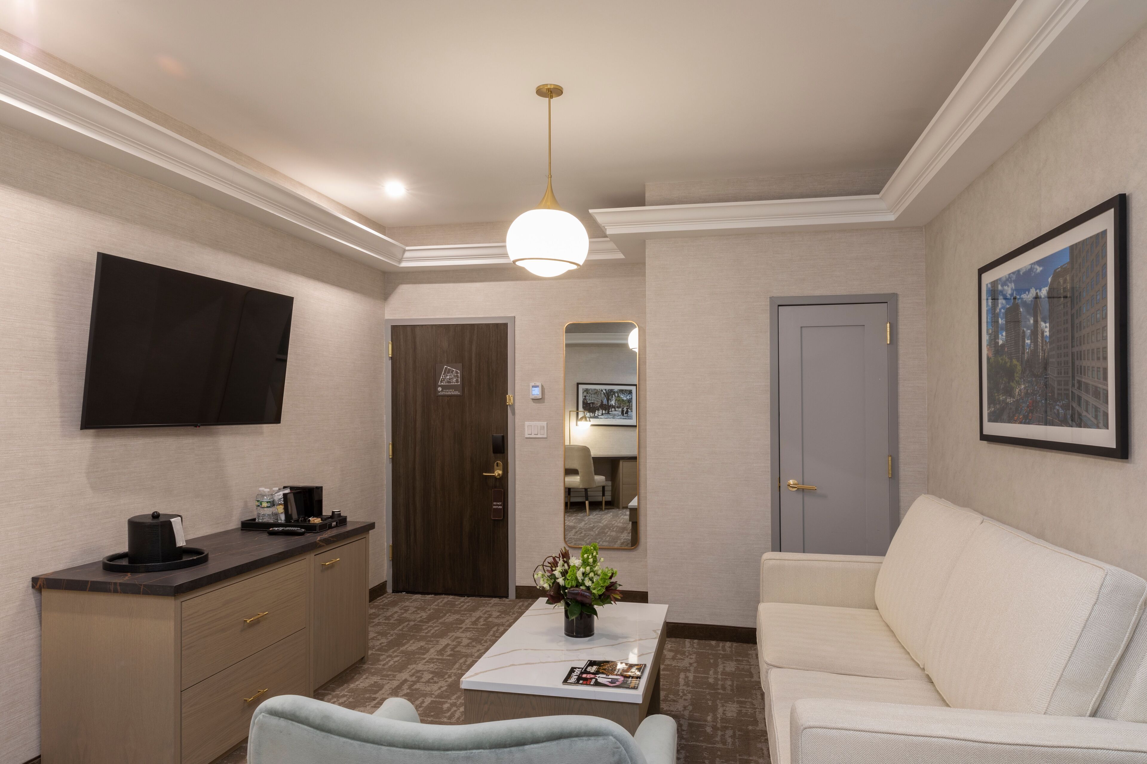 Un hall de hotel con un televisor de pantalla plana, una mesa de recepción, un sofá, una mesa de centro con una revista y un cuadro enmarcado en la pared.